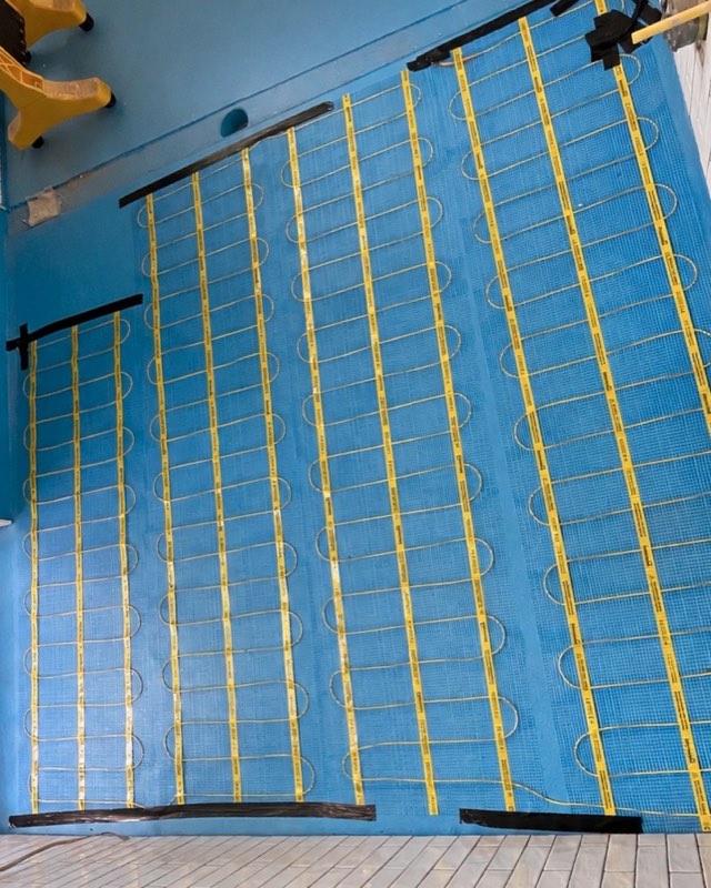 An electric underfloor heating mat laid across a bathroom floor before tiling